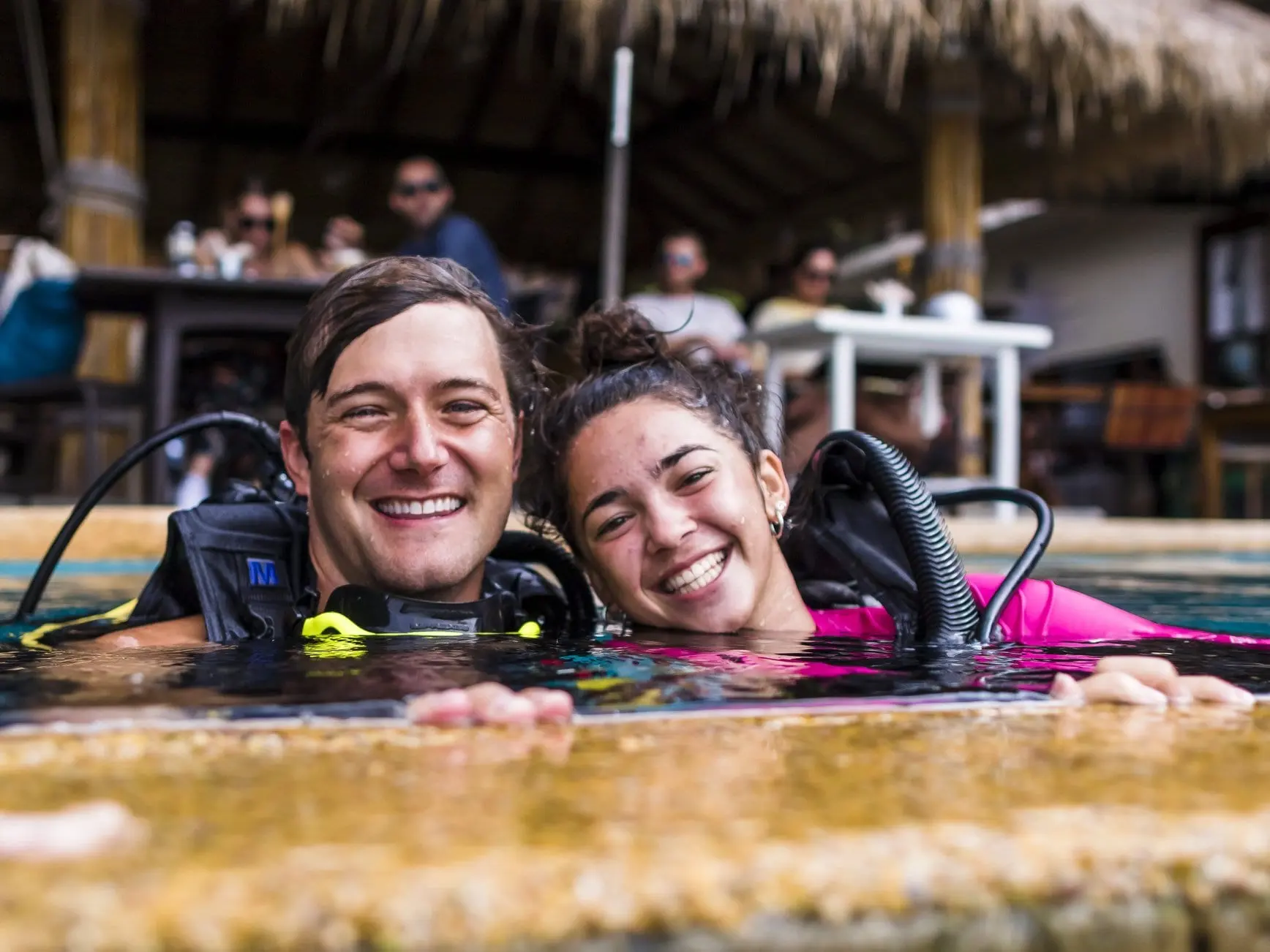 Co-founders Graham Patterson and Tamara Silverstone smiling in scuba gear at the edge of a pool during Divemaster training.