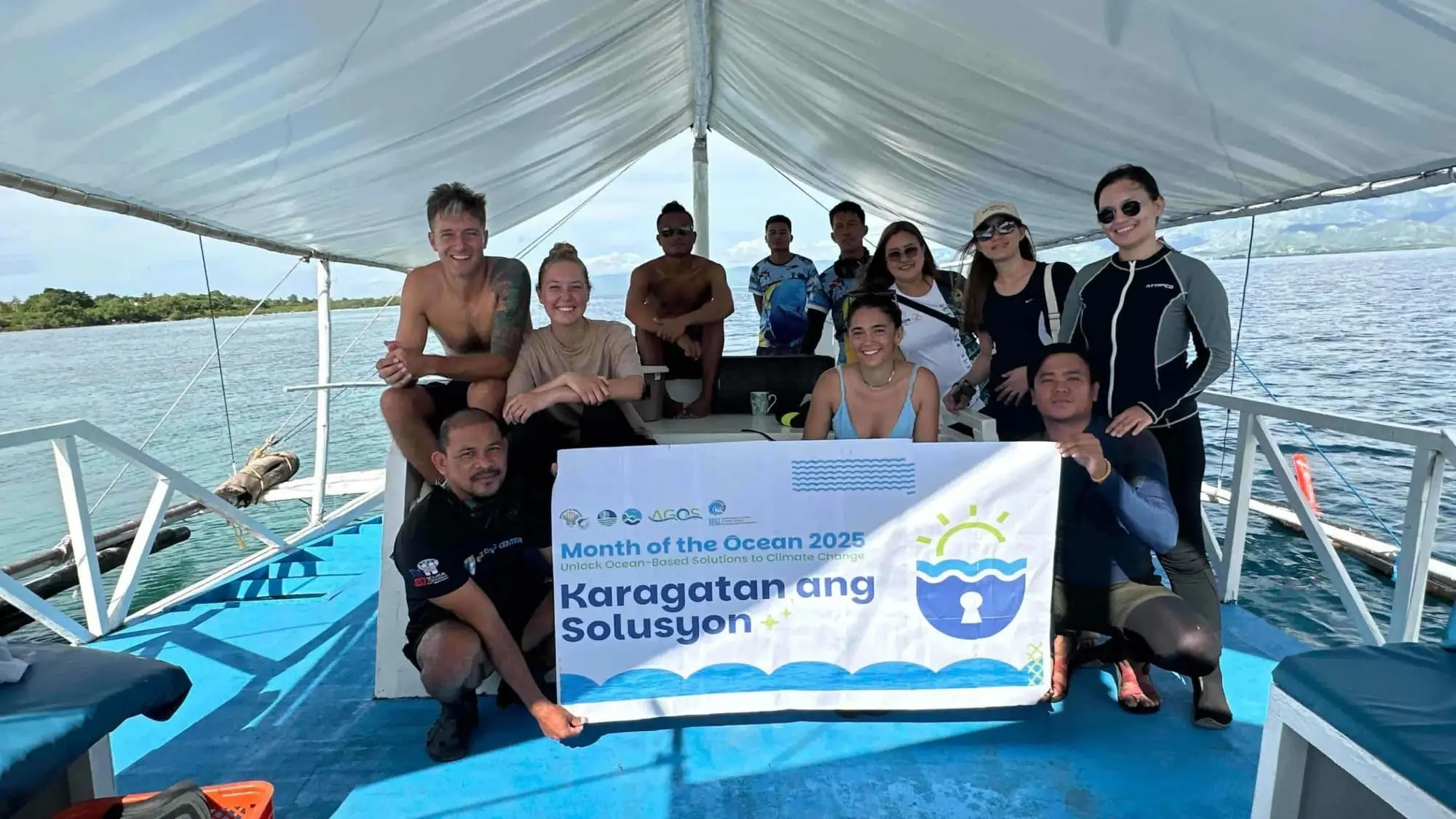 REEF Scuba team with local marine managers on a boat, holding a Month of the Ocean banner.